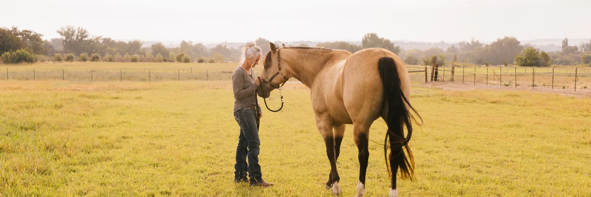 Kellie Robinson with her buckskin quarter horse in an open pasture