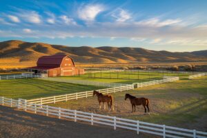 Aerial view of a horse property with white fencing, red barn, and green irrigated pastures set against golden high desert hills in Eastern Oregon