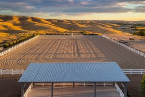 Aerial view of Eastern Oregon horse property showing both outdoor arena and covered riding facility at golden hour