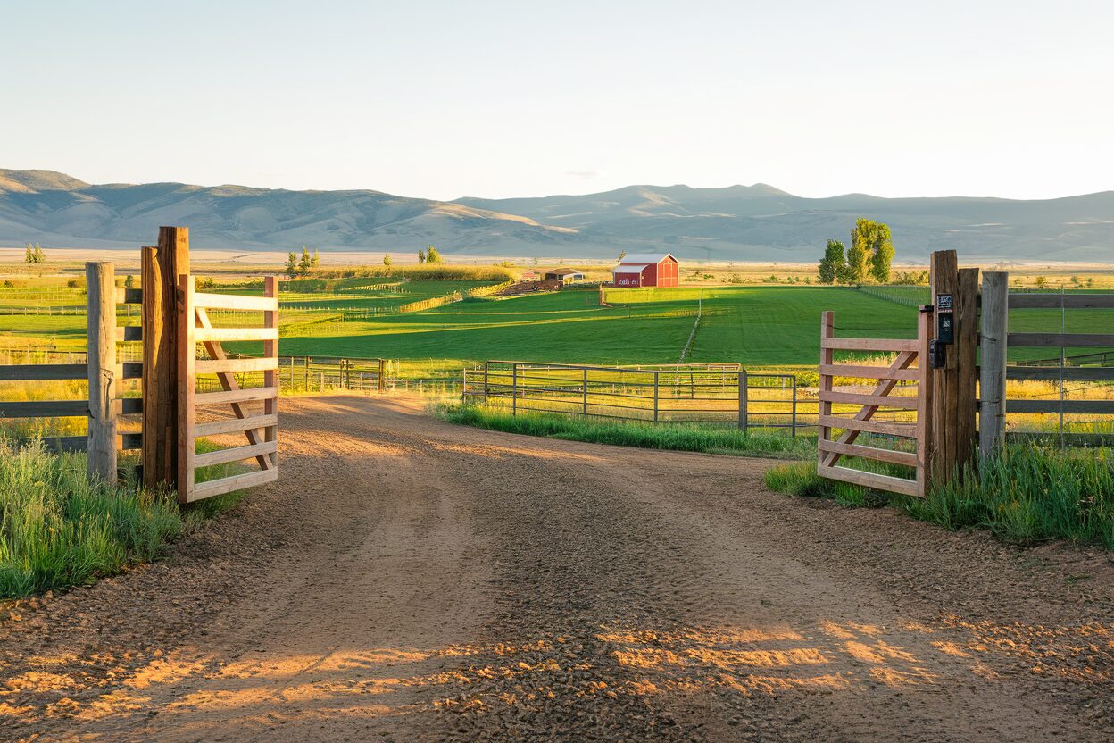 Rural Idaho ranch entrance with gravel driveway leading to green pastures and barn
